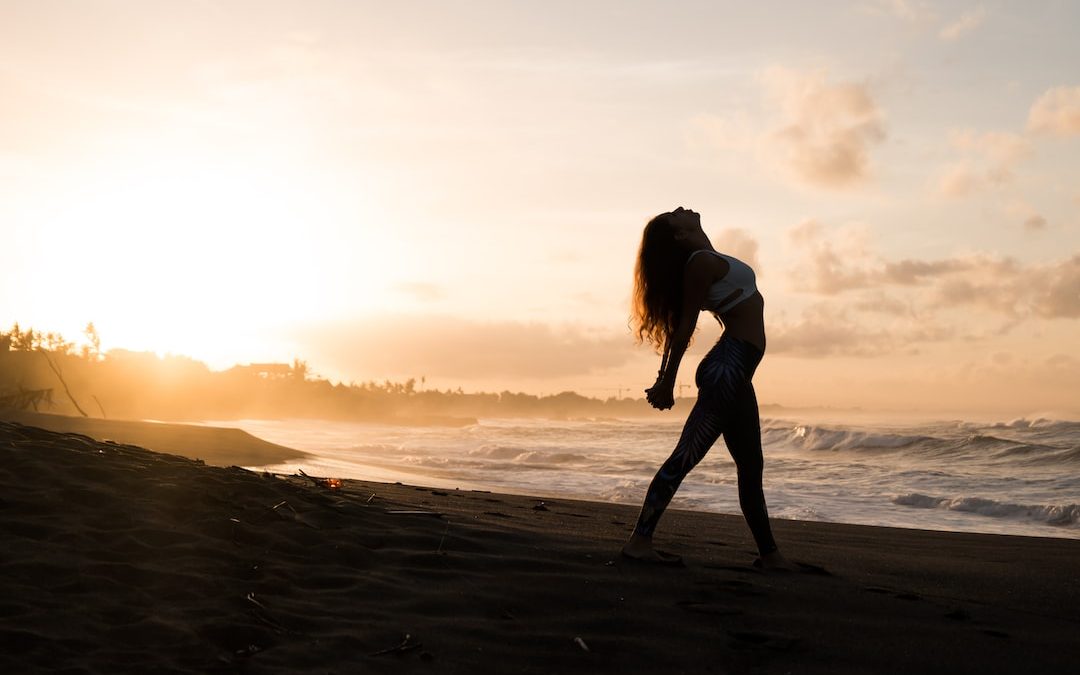 silhouette of woman stretching her arms on seashore during sunrise