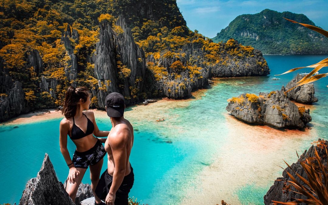 a man and a woman sitting on a rock looking at the ocean