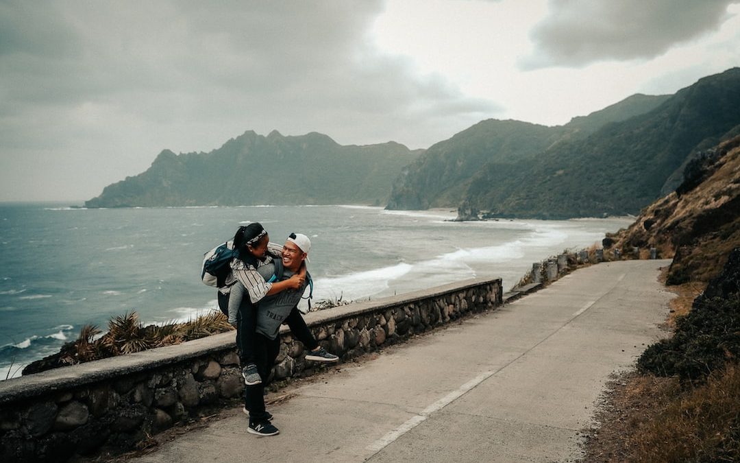 man and woman sitting on brown concrete fence near body of water during daytime