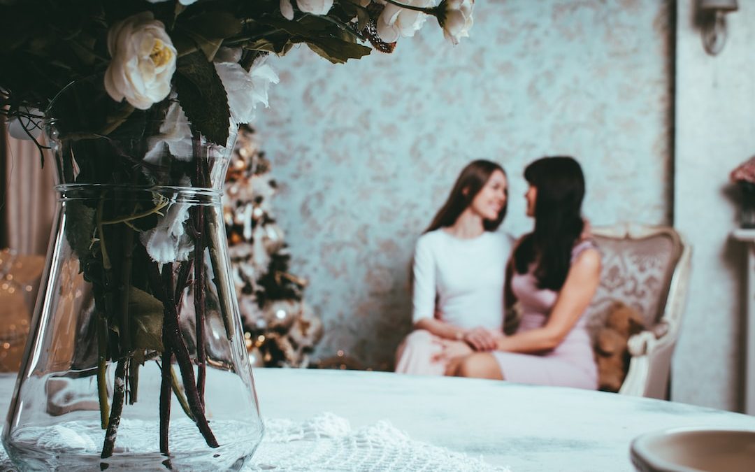 2 woman sitting on loveseatnear table with rose in vase