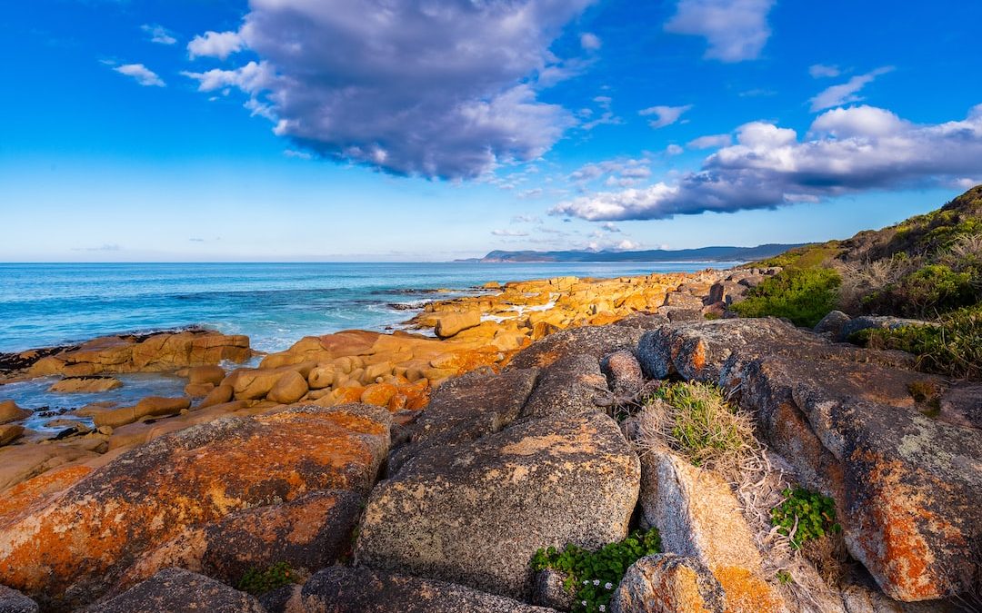a rocky beach with blue water and clouds
