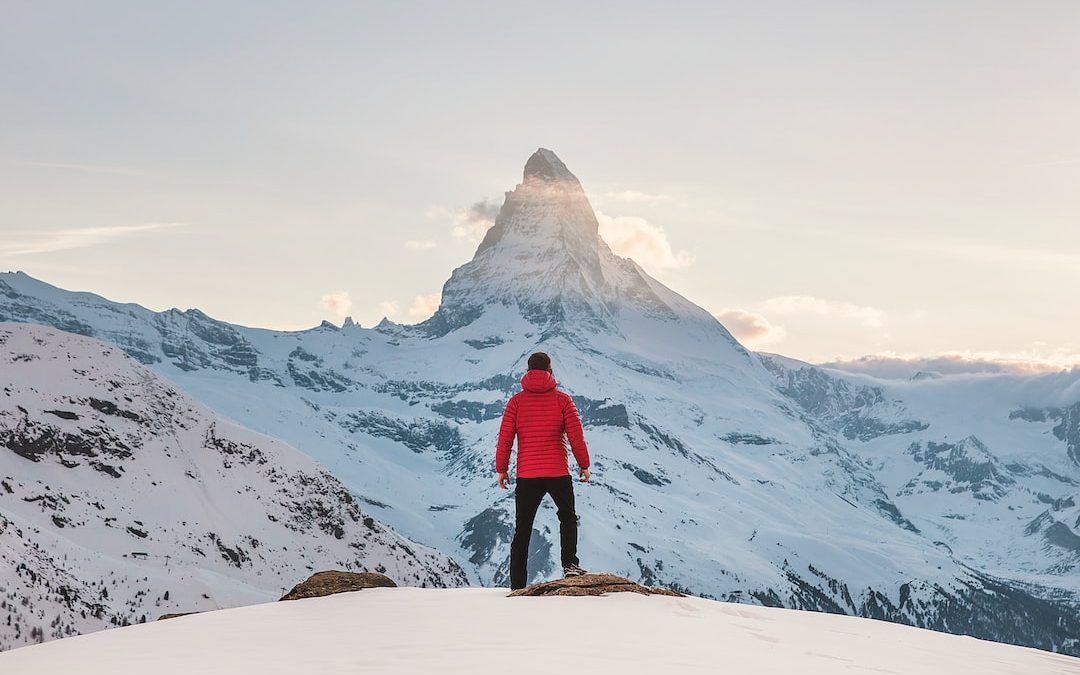 person in red hoodie standing on snowy mountain during daytime