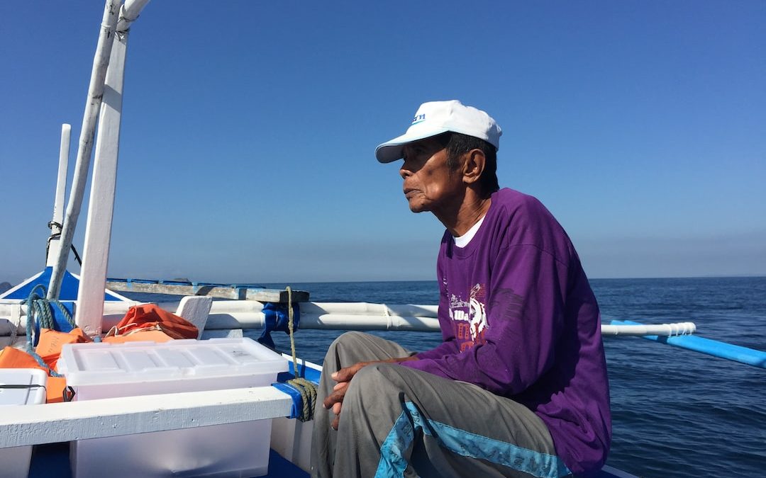 man in purple hoodie and gray pants sitting on boat during daytime