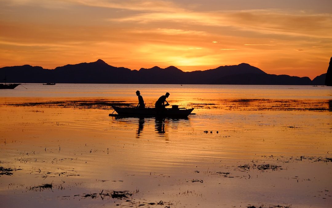 silhouette of two people riding boat on body of water during golden hour