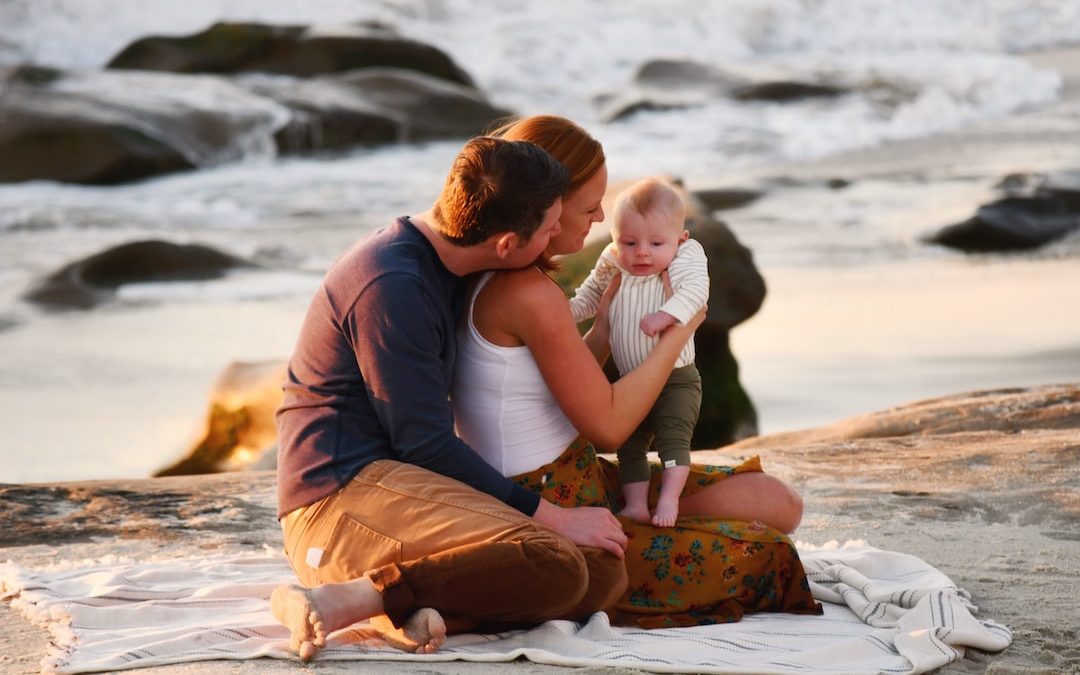 a man and woman sitting on a beach with a baby