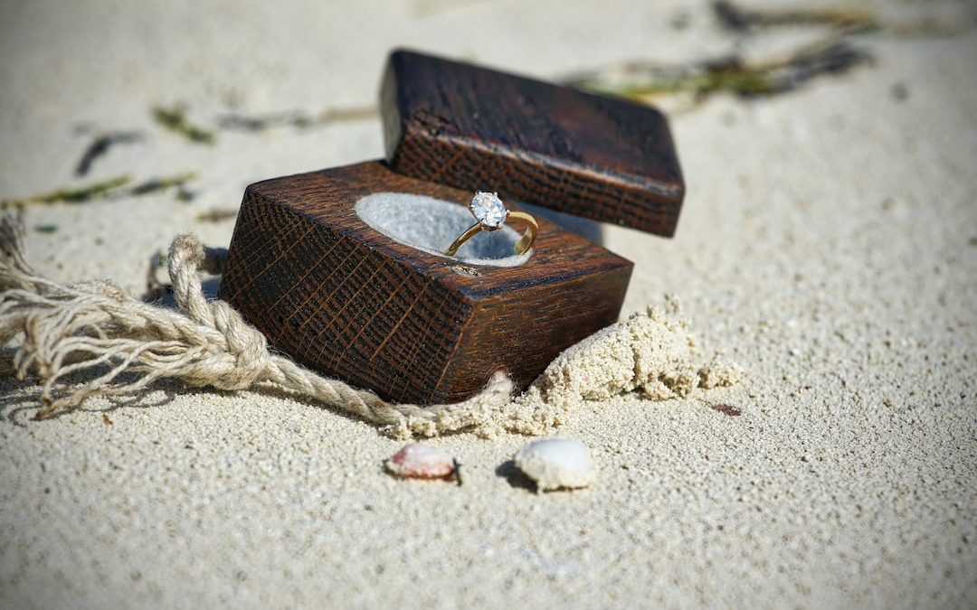 gold-colored clear gemstone ring in brown wooden box on sand