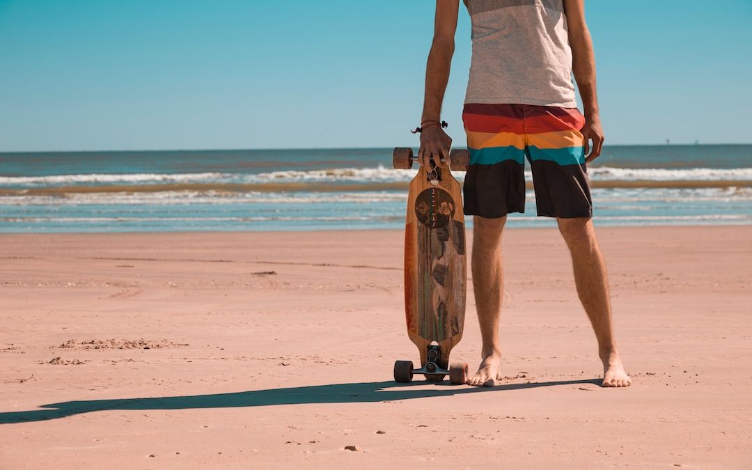 man holding longboard standing at sea shore