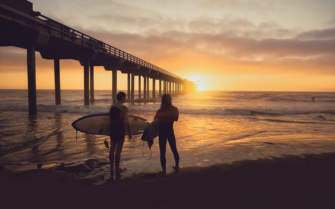 woman carrying surfboard beside person during sunset