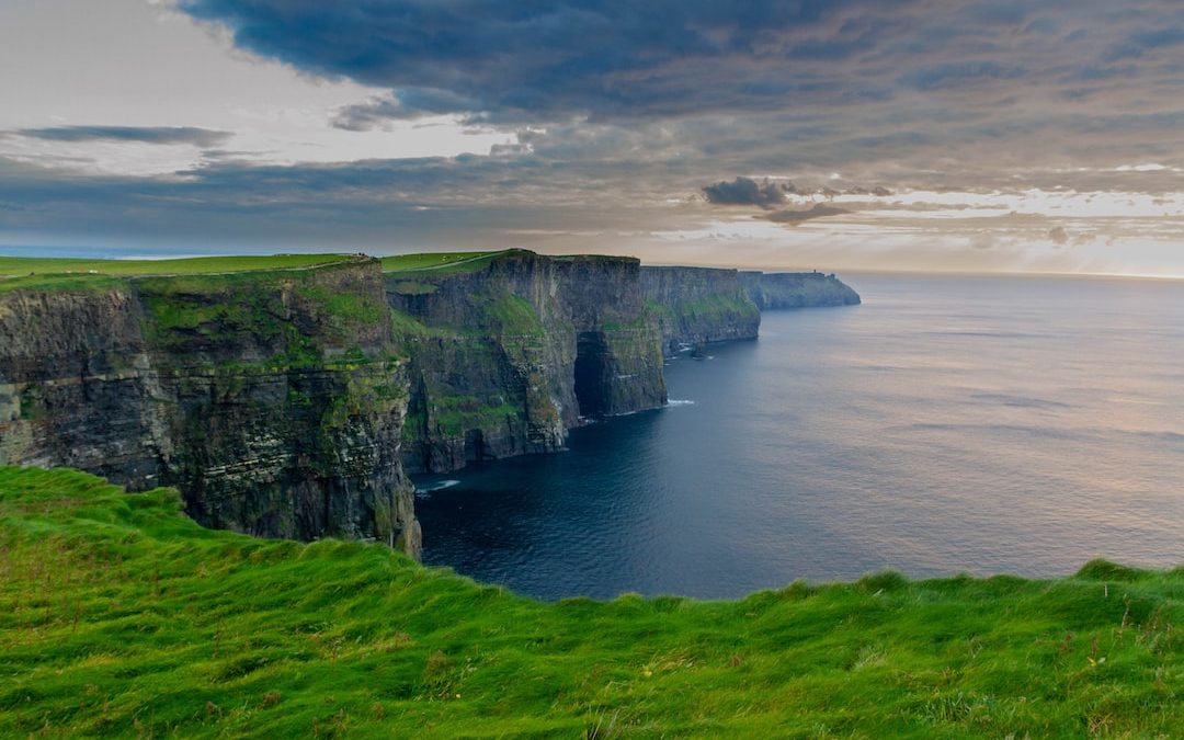 green grass field beside body of water under cloudy sky during daytime