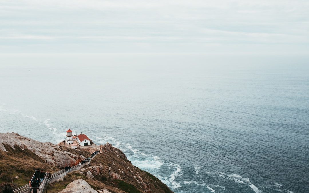 house and lighthouse near cliff and body of water aerial photography