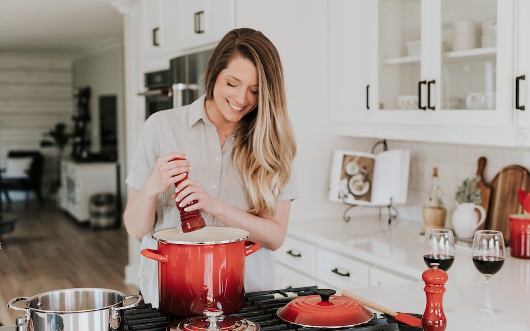 smiling woman standing and putting pepper on stock pot
