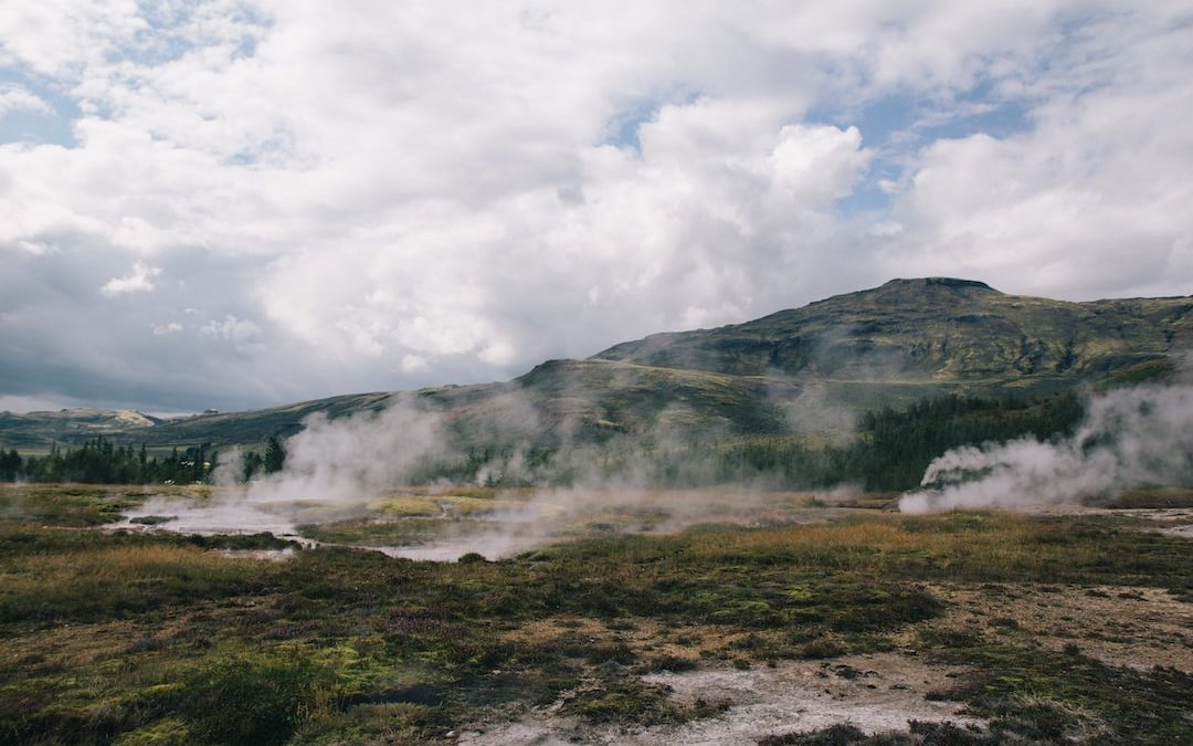 steam rises from the ground in front of a mountain