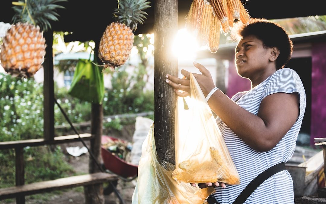 woman holding yellow plastic bag near pineapple fruits