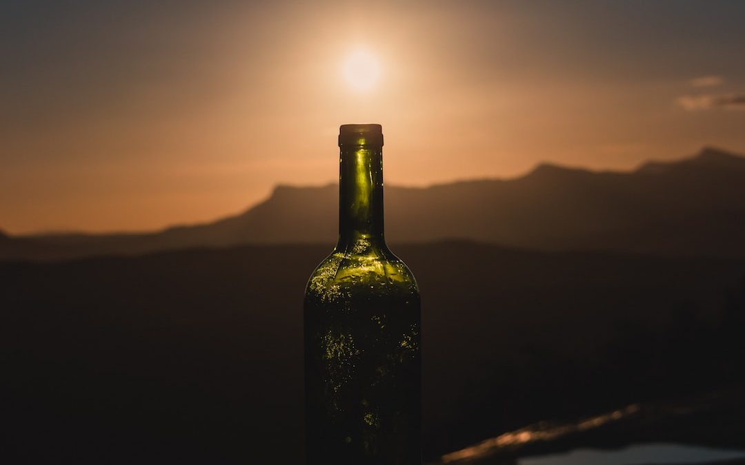 green glass bottle on brown wooden table during sunset