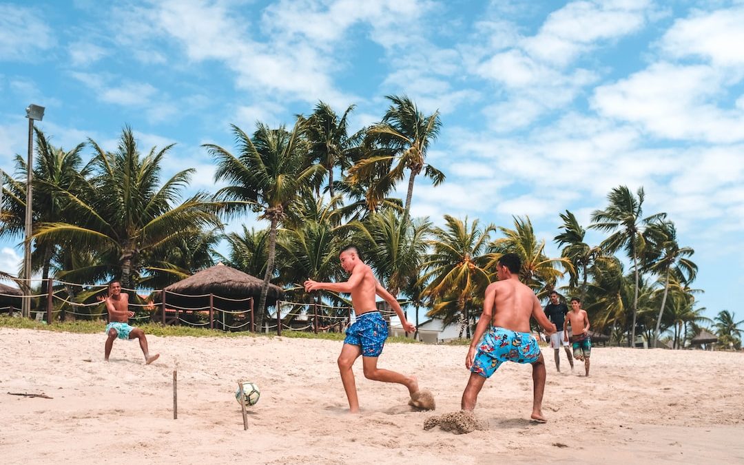 several men playing football on beach sand