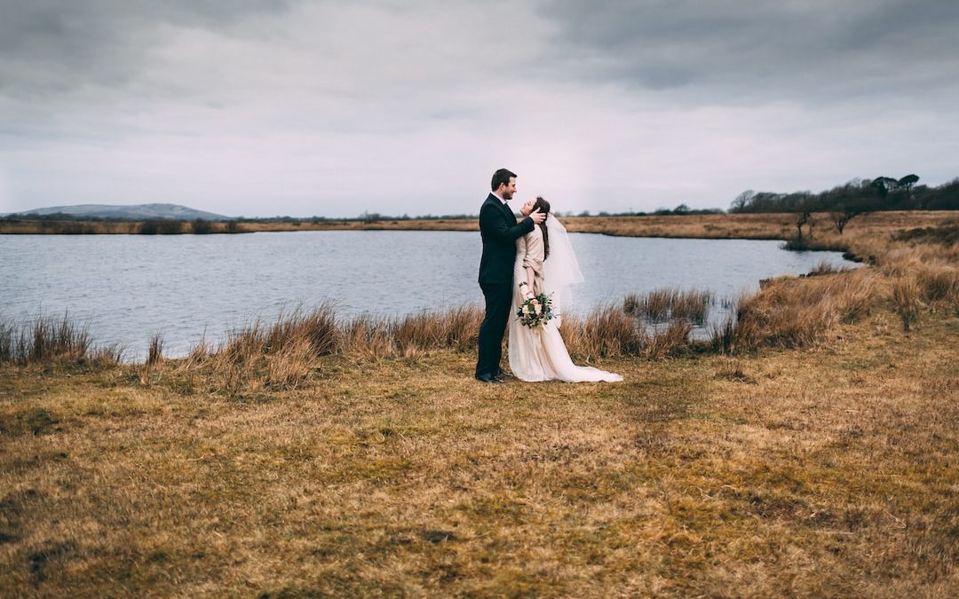 bride and groom photography on brown grass near body of water during daytime