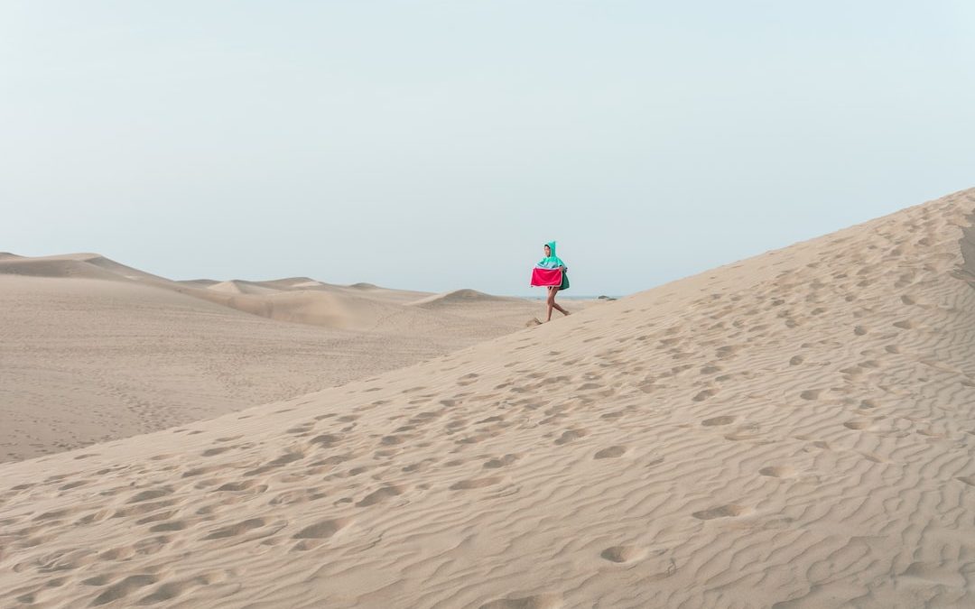 photo of person walking on desert holding red box