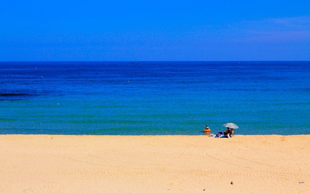 person on beige seashore near blue ocean under clear blue sky at daytime