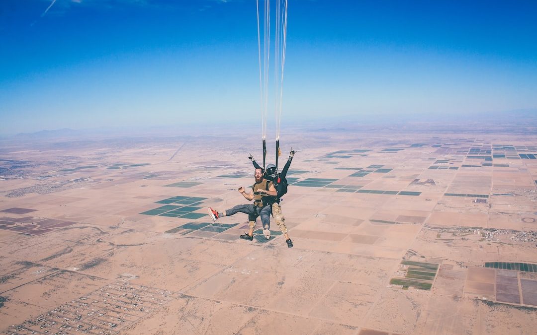 two men in 1 parachute in mid air during daytime