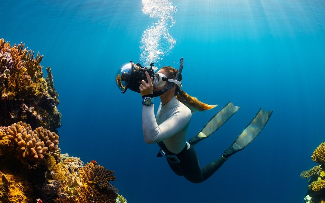 a woman scubas in the ocean with a camera