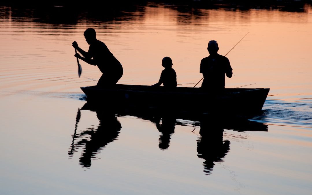 silhouette of three person riding on boat on body of water
