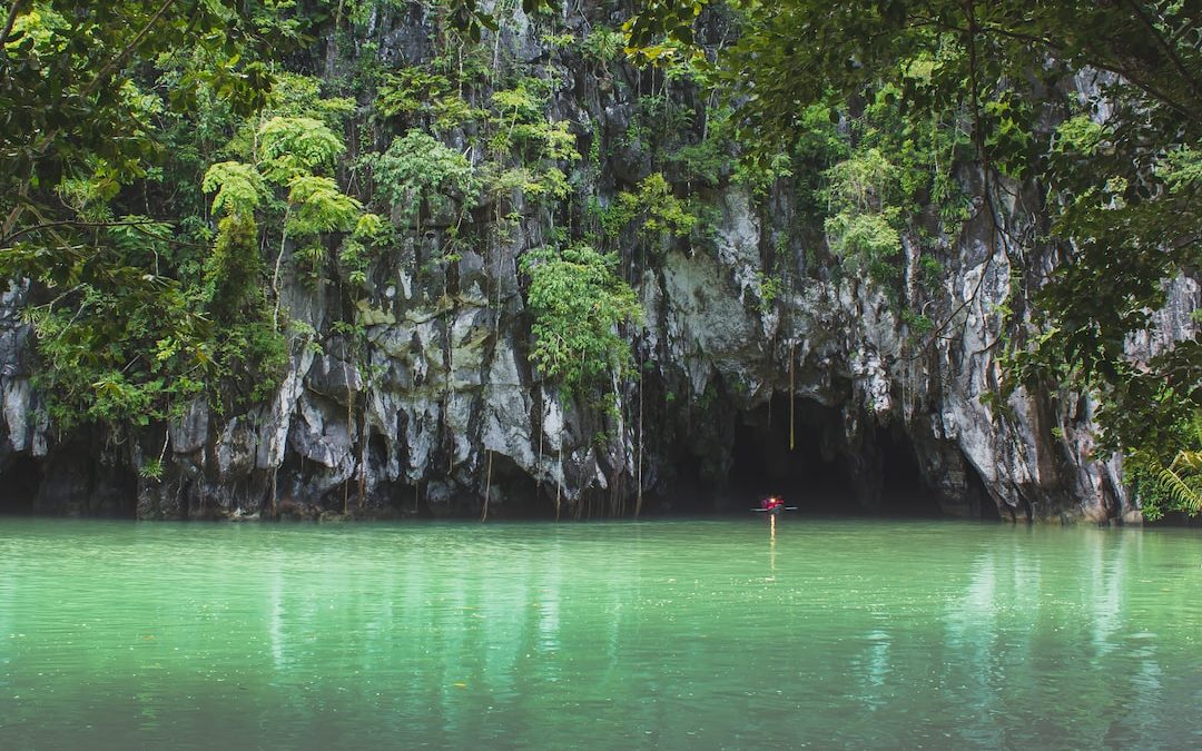 person in red shirt standing on rock in the middle of lake during daytime