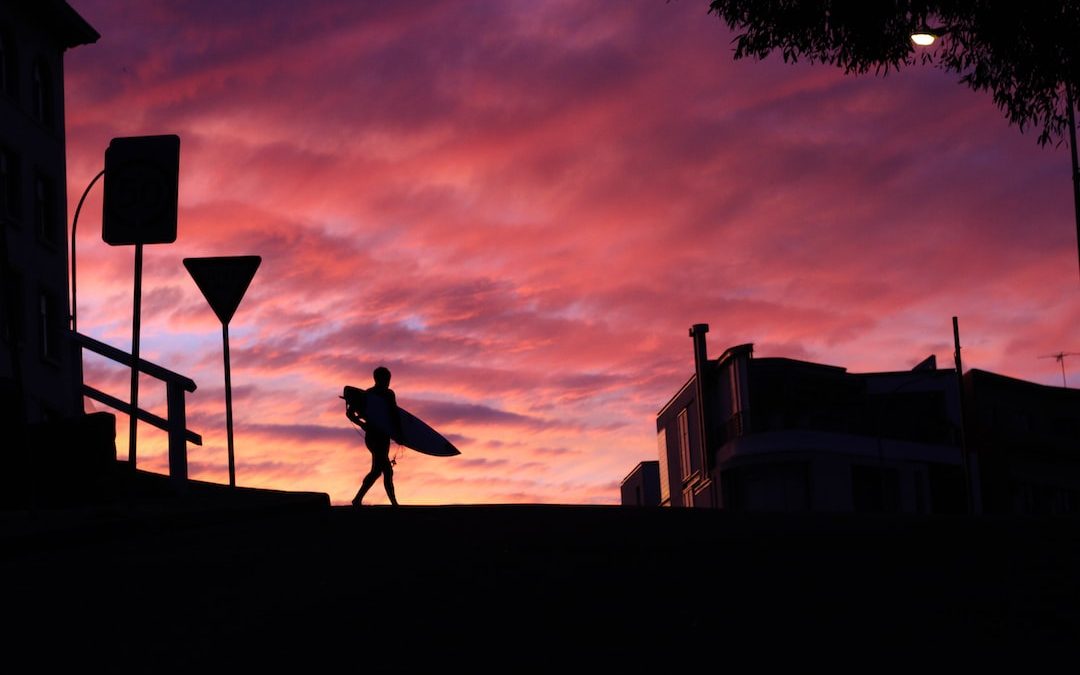 silhouette photography of man walking with a surfboard