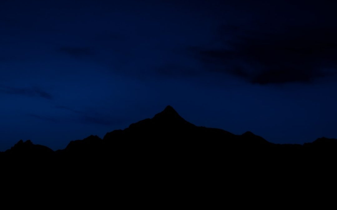 the silhouette of a mountain against a dark blue sky