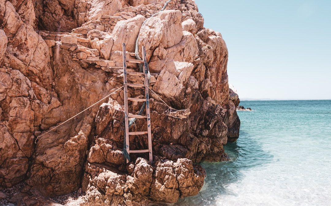 brown wooden ladder on brown rock formation near body of water during daytime