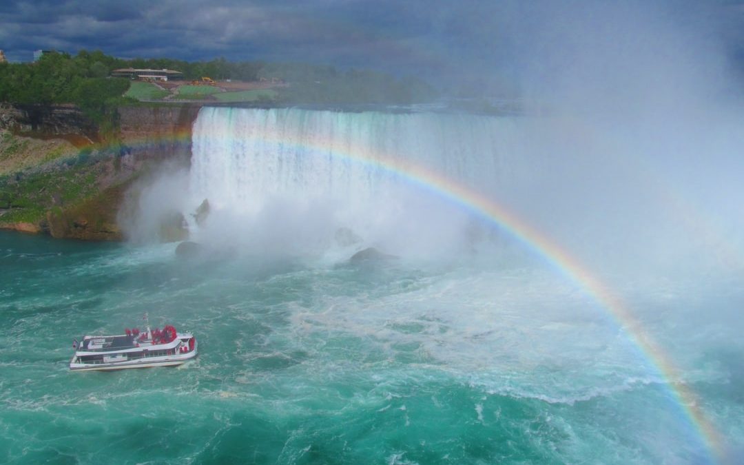 white and black fishing boat in blue ocean water under rainbow during daytime