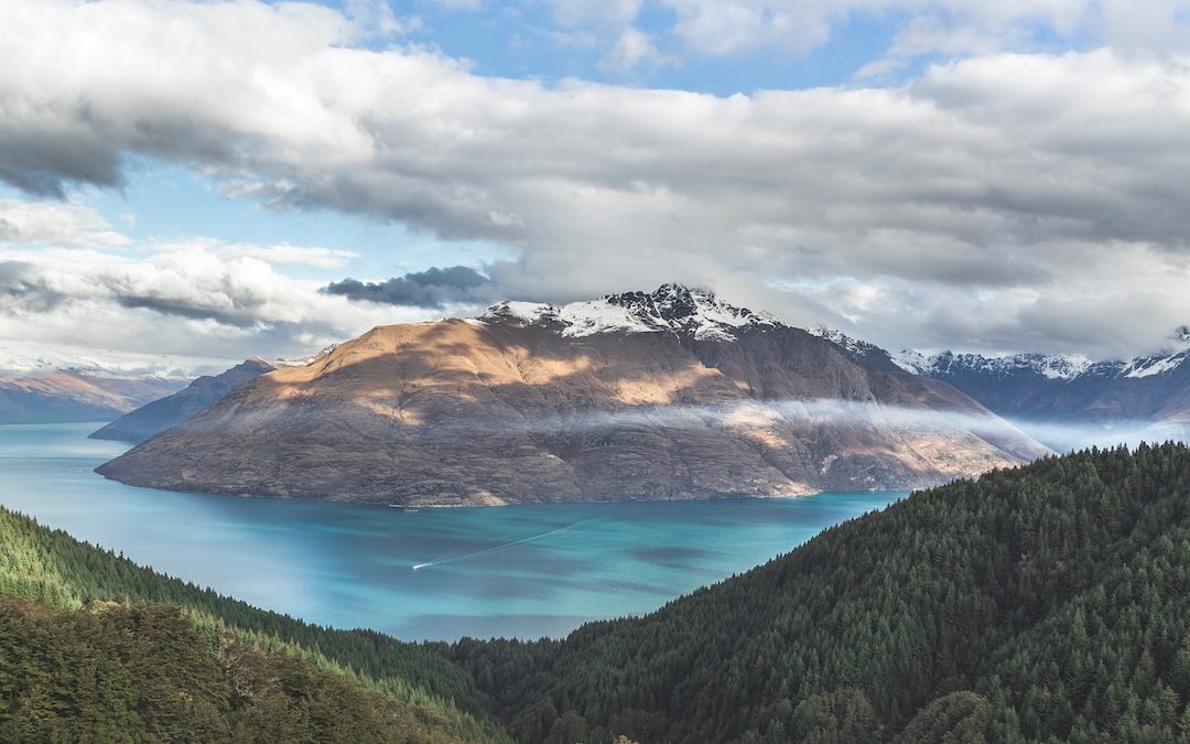 landscape photography of mountain under cloudy sky between body of water at daytime