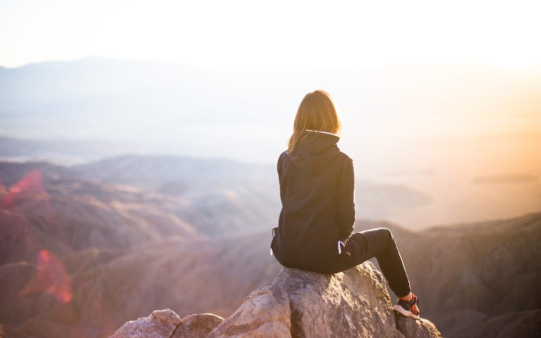 person sitting on top of gray rock overlooking mountain during daytime