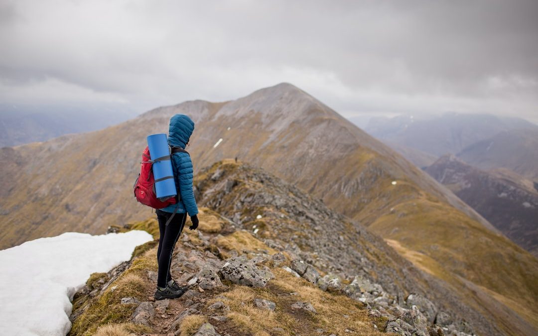person at peak of mountain carrying red backpack