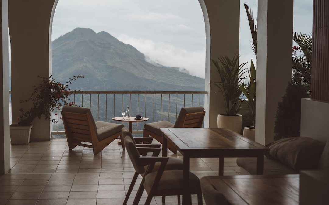 a patio with chairs and tables and a body of water in the background