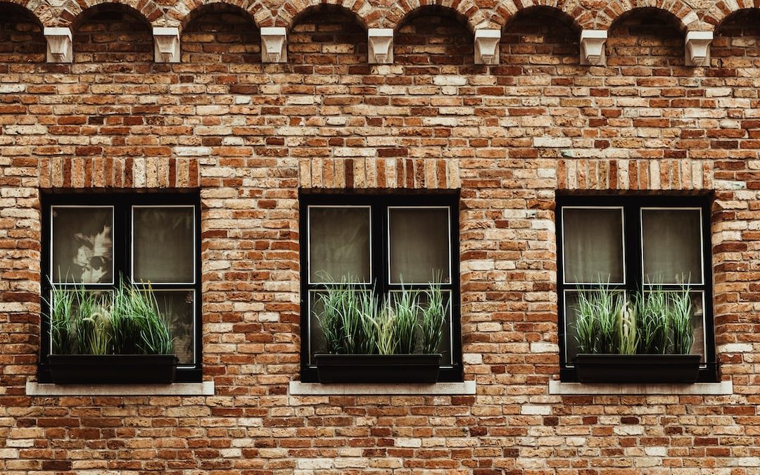 a brick building with three windows with plants in them