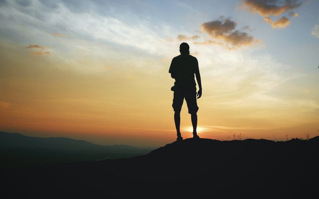 silhouette of man standing on top of mountain during sunset