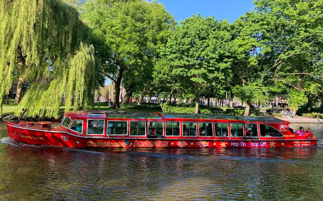 red passenger boat beside green leafed trees