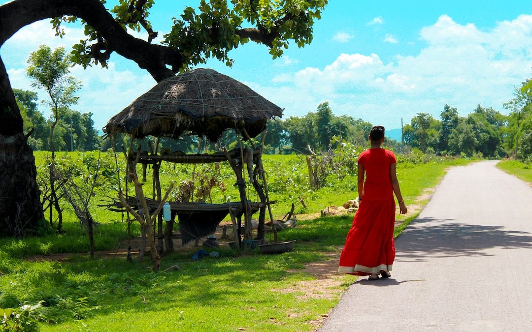 woman in red dress walking on pathway near brown wooden gazebo during daytime