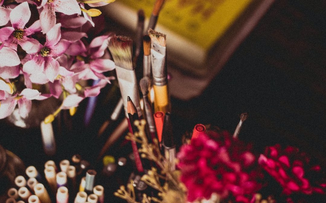 selective focus photography of makeup brush and pencil and pens beside pink and purple flowers