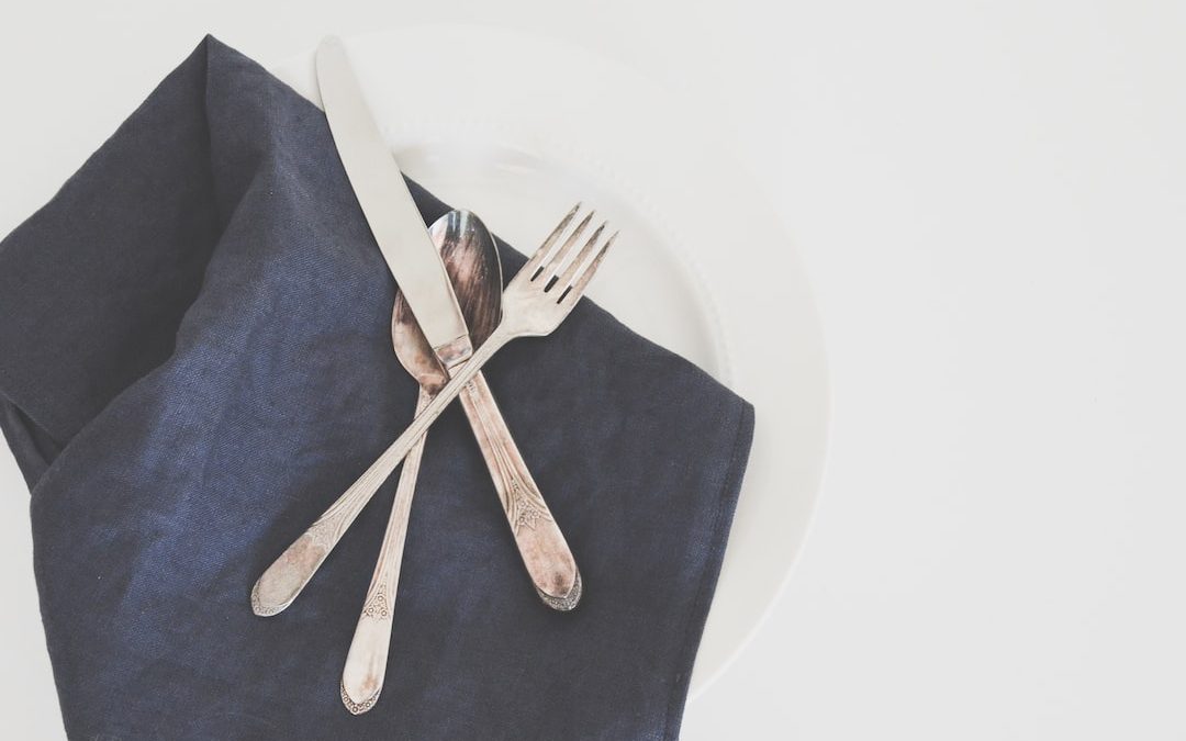 gray fork, spoon, and butter knife on plate with black table napkin