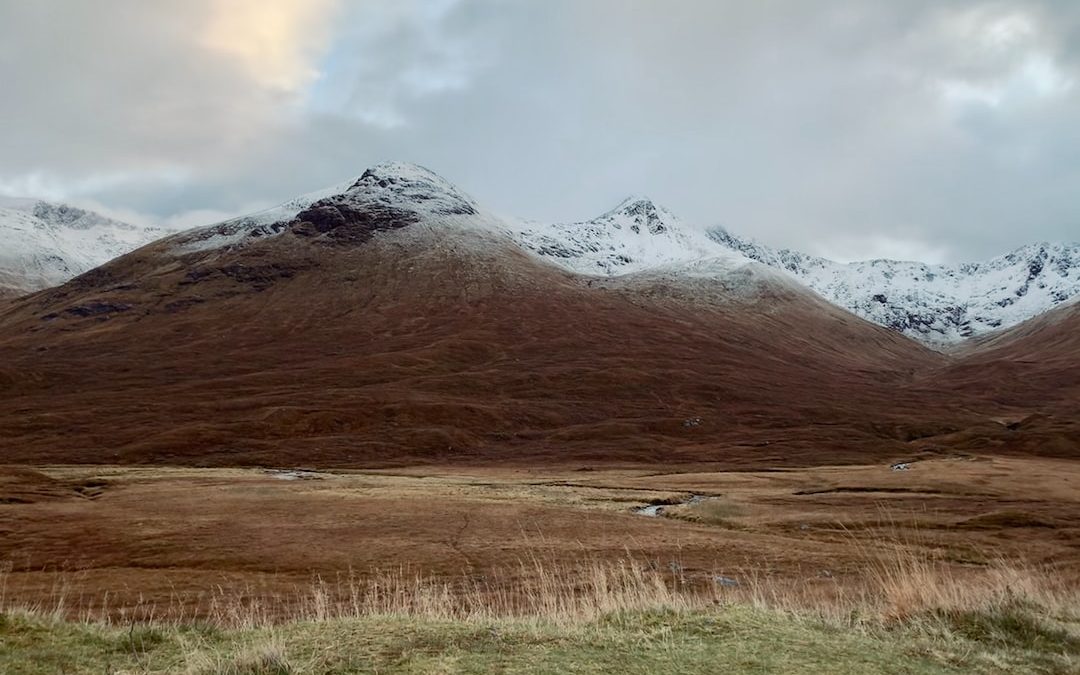 brown grass field near snow covered mountain during daytime