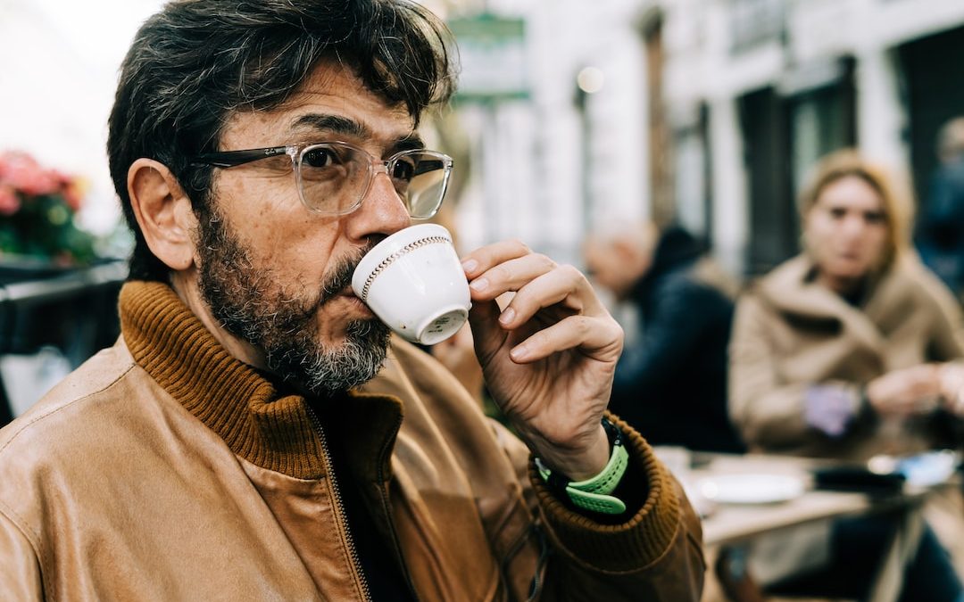 man in brown jacket drinking on white ceramic mug