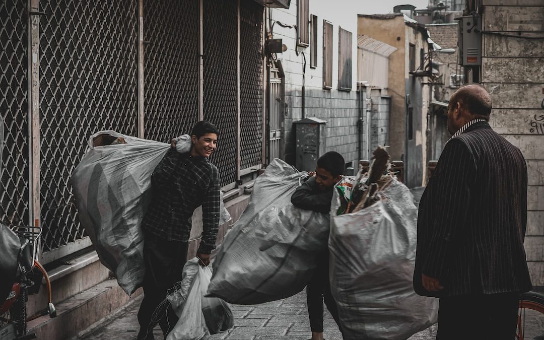 man in black jacket and gray pants holding black plastic bag