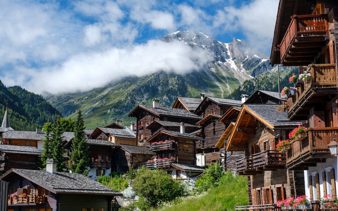 brown wooden houses near green trees and mountain under white clouds during daytime