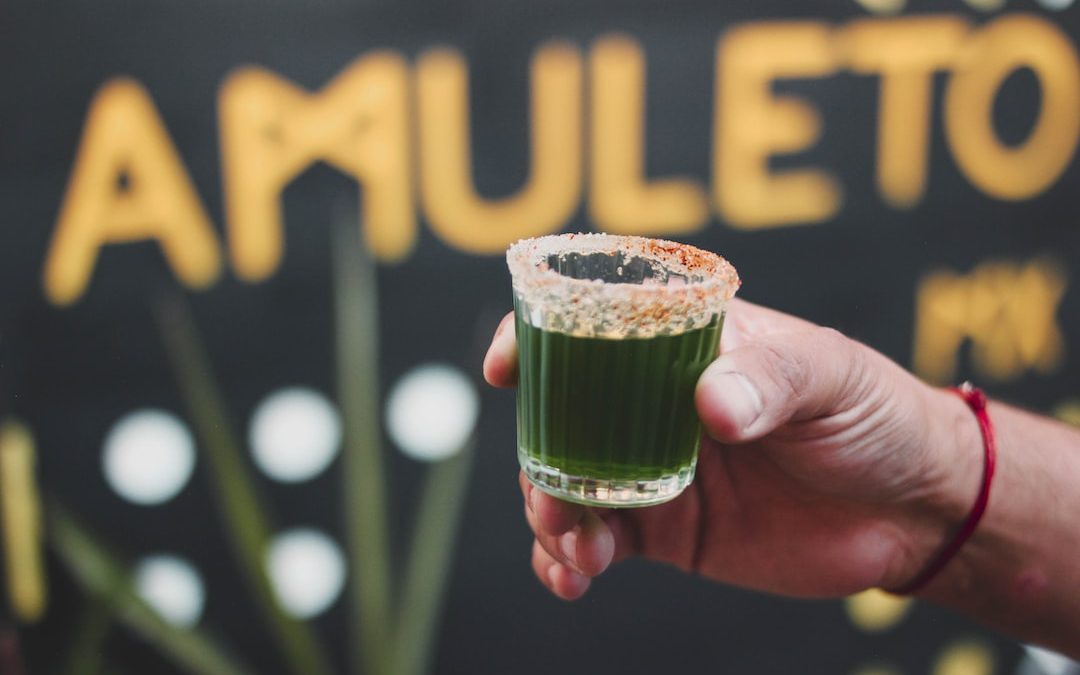 a person holding a green drink in front of a sign