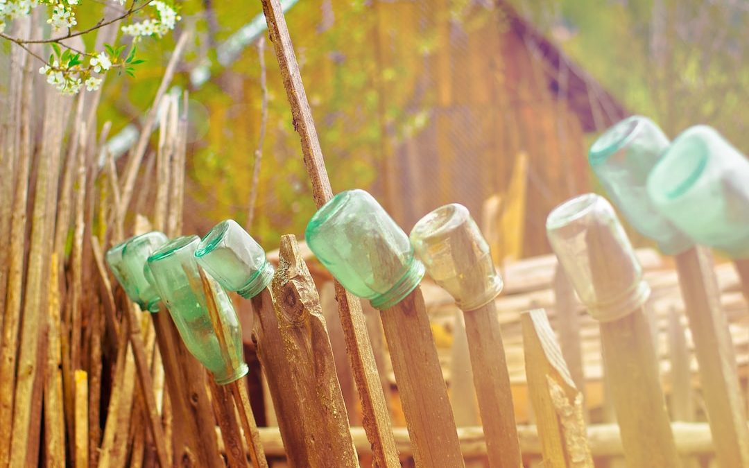 green glass jars on brown wooden fence