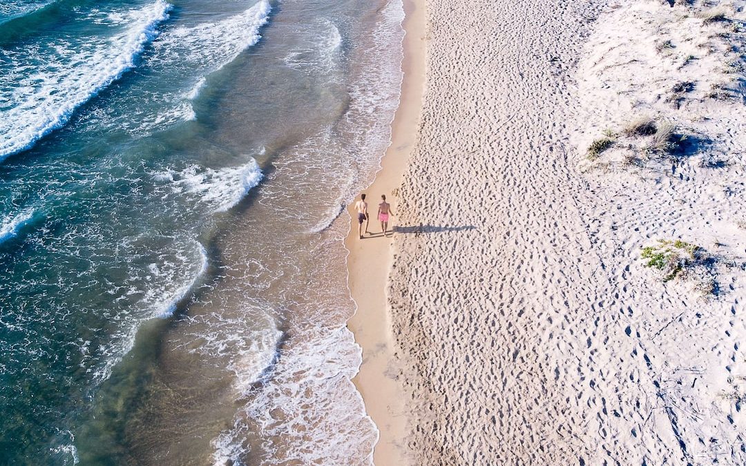 aerial photography of two person walking on seashore during daytime