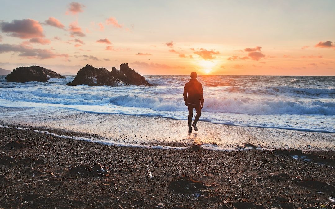 man walking in beach during golden hour