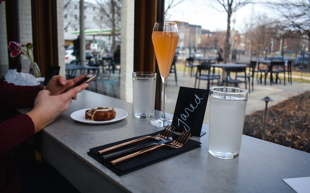 person holding smartphone near long-stem drinking glass