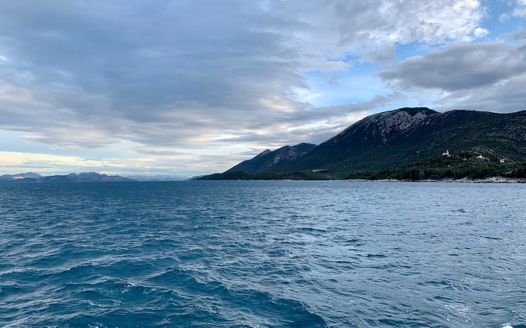 body of water near mountain under cloudy sky during daytime